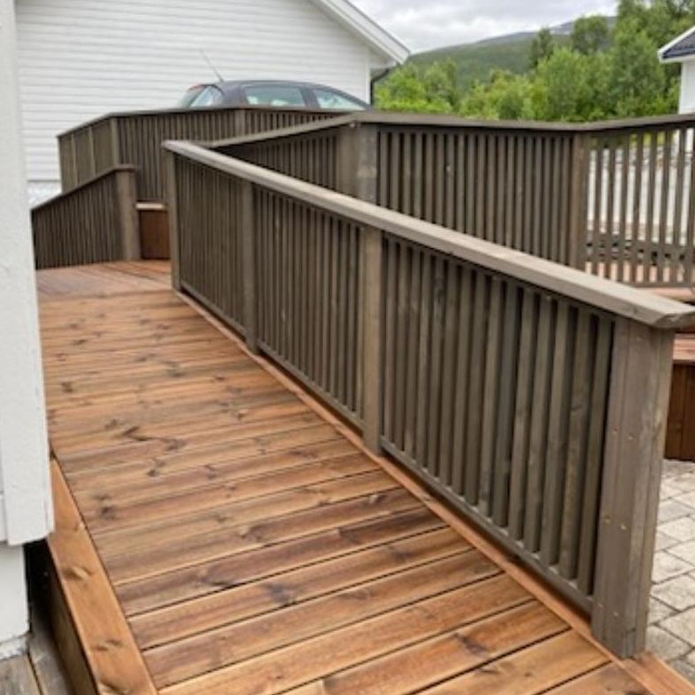 Rampe i tre med rekkverk leder opp til terrasse ved hvitt hus i boligområde.